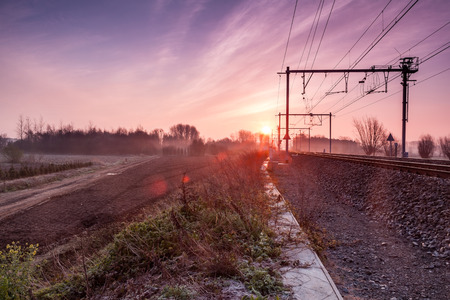 on an early morning at sunrise right next to a passing train with fog banks in the distanceの写真素材