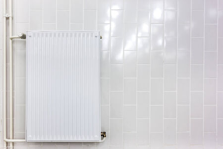 At the white tiles hang an radiator and tubesの写真素材