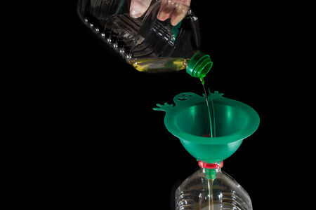 old frying oil pouring into another bottle with a green funnelの写真素材