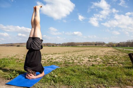 on an sunny day this man enjoys Mukta Hasta Sirsasana yoga in nature