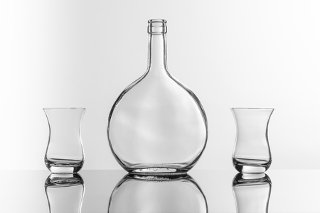 On a reflective tile is an empty transparent bottle and glassの写真素材