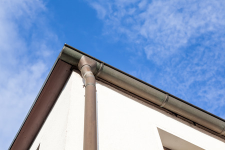 an rain drain pipe from the roof whit blue sky and cloudsの写真素材