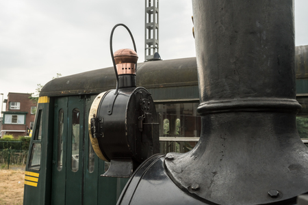 in an old train station there is an old steam train with a large oil lamp in front of his chimney