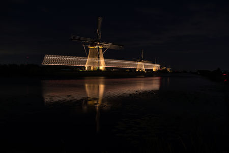 During night in the evening the world famous Kinderdijk in the Netherlands with the windmills illuminated, there are also light stripes of boatの写真素材