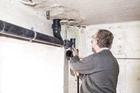 Underneath the ceiling in a vase room hang drain pipes of toilets under construction