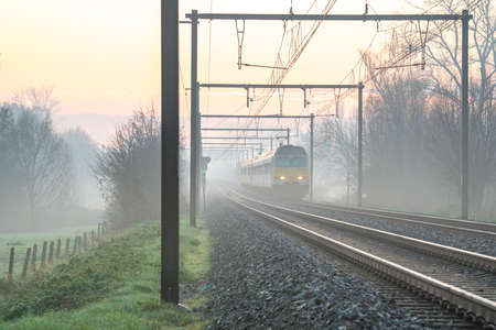 On a beautiful morning on the track with an train and the sun rising with ground fog and without a cloud in the skyの写真素材