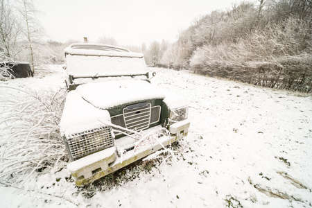 on a meadow there is an abandoned car with snowの写真素材