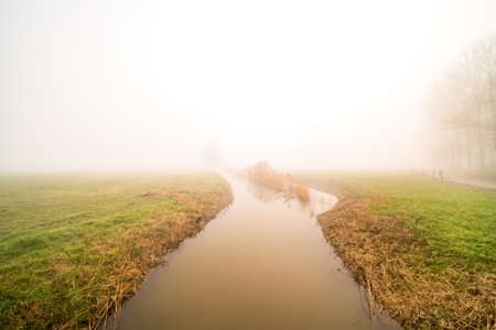 A river running through the meadow on a foggy winter morningの写真素材