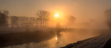 Early on a frosty morning with fog rising along a river with several bendsの写真素材
