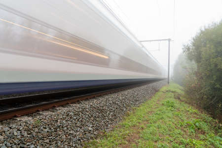 On a beautiful foggy morning along the track, a passenger train rages byの写真素材
