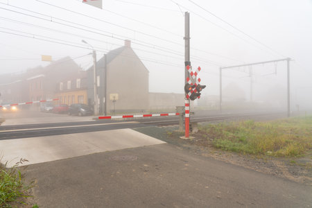 On a foggy morning along this transition of the track with barrier and lights, a passenger train rages byの写真素材