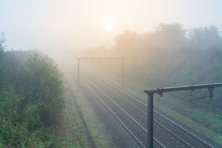 On a Foggy morning on the track with overhead lines and a rising sun