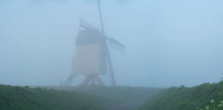 Early in the morning there is a beautiful windmill in the mist whit the sun rising in the skyの写真素材
