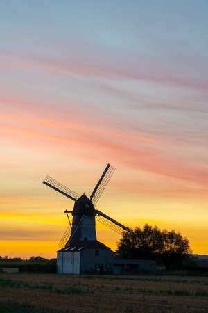 Early in the morning there is a beautiful windmill whit the sun rising in the skyの写真素材