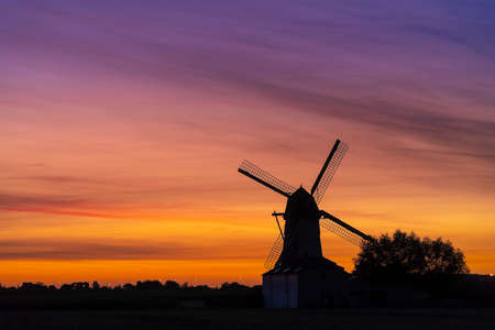 Early in the morning there is a beautiful windmill whit the sun rising in the skyの写真素材