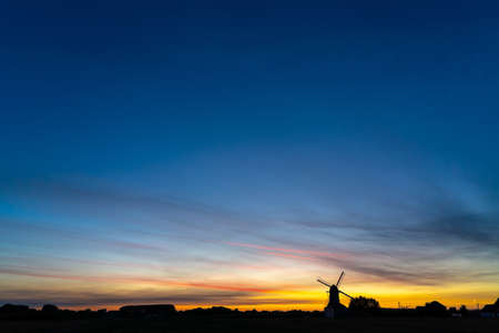 Early in the morning there is a beautiful windmill whit the sun rising in the skyの写真素材