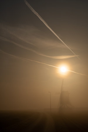Early in the morning there is a beautiful windmill in the mist whit the sun rising in the skyの写真素材