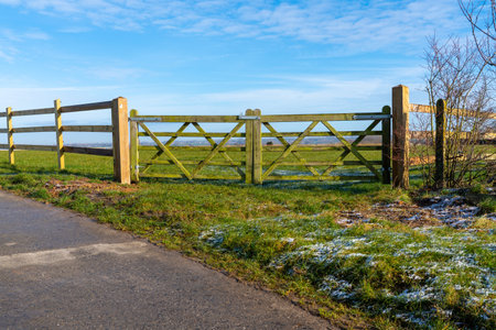 At the edge of the meadow there is wooden fence next to a road that goes down a lane through the landscapeの写真素材
