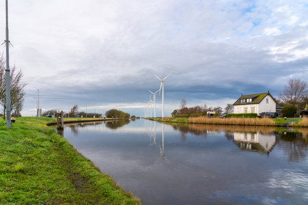Windmills stand in a row next to a river on a sunny dayの写真素材