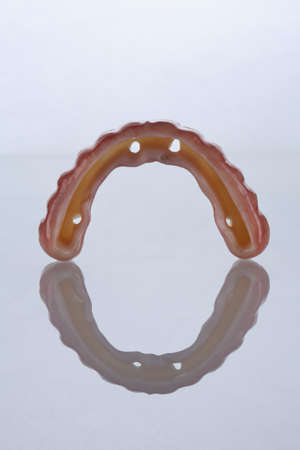 Dental prosthesis from zircon with a hole for titanium beam, on a white background with reflection