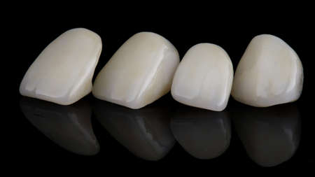 four dental crowns for central teeth made of ceramic on a black background