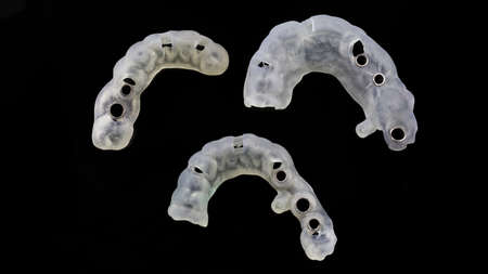 three dental templates made of polymer for large implantation, shot from above on a black background