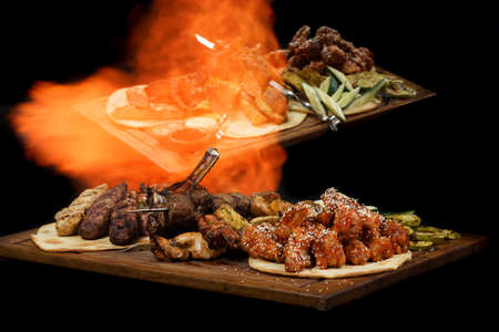 different types of meat dishes on a board with fire and reflection on a black backgroundの写真素材