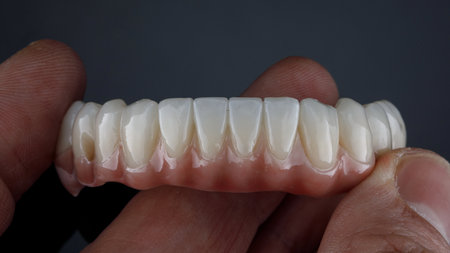 dental prosthesis made of ceramics and titanium of the lower jaw in the doctor's hand on a black...