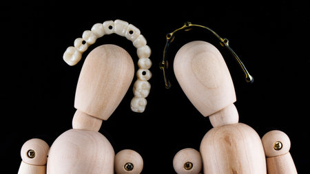 two wooden people with dental prostheses and a beam on a black background