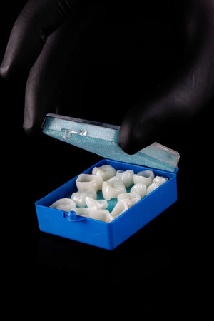 Doctor's hand in a black glove, opens a blue case with ceramic dental crownsの写真素材