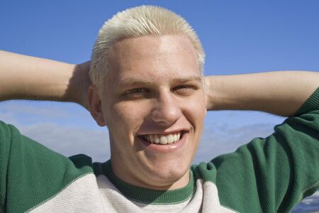 A smiling young man with arms behind his headの写真素材