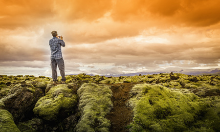 A tourist snapping a photo of moss covered lava rocks in Vatnajokull National Park, Iceland