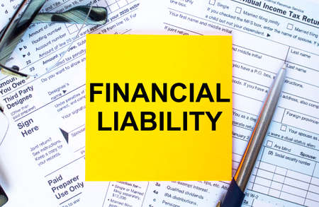 Financial concept. Text Financial Liability on note paper with the U.S IRS 1040 form,pen and glassesの写真素材