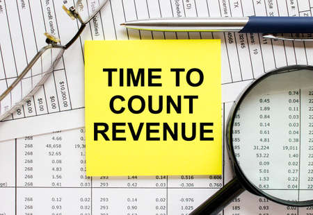 Text Time To Count Revenue on financial tables with pen, glasses and paper clips. Business and financial conzeptの写真素材