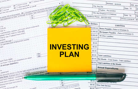 Text Investing Plan on note paper with pen, compass and paper clips. Business and financial conzept