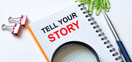 Notepad with text Tell Your Story on white background with clips, pen and magnifying glass. Business and financial conzeptの写真素材