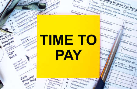 Financial concept. Text Time To Pay on note paper with the US IRS 1040 form, pen and glassesの写真素材