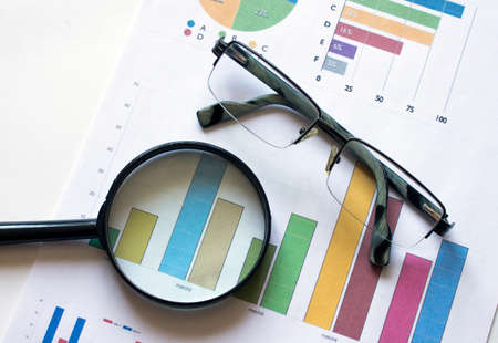Magnifying glass with glasses on working paper with diagram