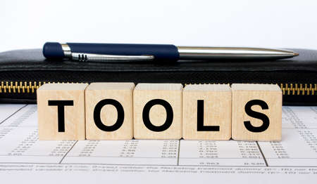 A word Tools written in a wooden cube with a pen and walletの写真素材