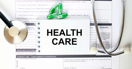 Text Health Care in a notebook on medical forms with a phonendoscope and green pillsの写真素材