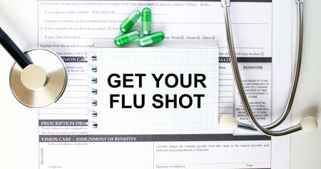 Text Get Your Flu Shot in a notebook on medical forms with a phonendoscope and green pillsの写真素材