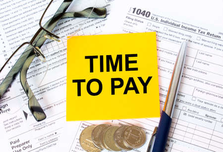 Tax-filling concept. Text Time To Pay on note paper with the US IRS 1040 form, pen and glassesの写真素材