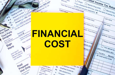 Financial concept. Text Financial Cost on note paper with the US IRS 1040 form, pen and glassesの写真素材