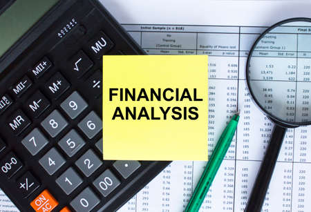 Sticker with text Financial Analysis lying on the calculator. Magnifying glass with green pen on financial documents. Business and financial conceptの写真素材