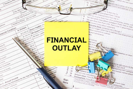Yellow sticker with text Financial Outlay. Next to it is a blue pen with colored stationery clips and eyeglasses. It can be used as a business and financial conceptの写真素材