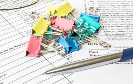 A blue metal pen sits on the financial tables with multi-colored stationery clips and eyeglasses. Business and financial conceptの写真素材