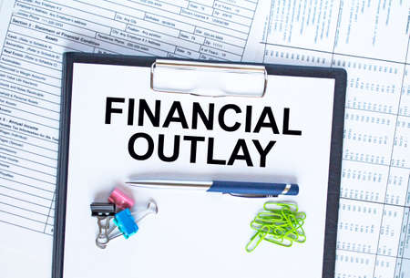 Text Financial Outlay on the folder that is located on the financial reports with calculator and stationery clips. Business and financial conceptの写真素材