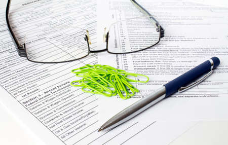 A blue metal pen sits on the financial tables with green paper clipsand eyeglasses. Business and financial conceptの写真素材