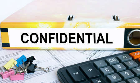 Text Confidential on the folder that is located on the financial reports with calculator and stationery clips. Business and financial conceptの写真素材