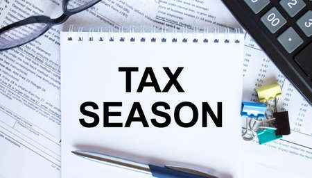 Notepad with text Tax Season, paper clips, blue pen, eyeglasses on financial diagrams. Business conceptの写真素材